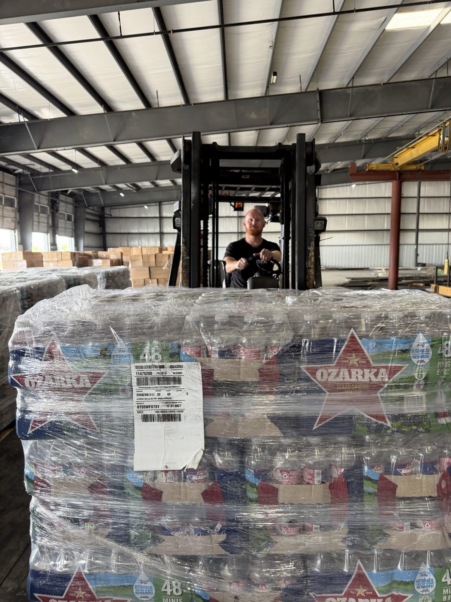A shrink-wrapped pallet of Ozarka bottled water in a warehouse, with a forklift operator behind it